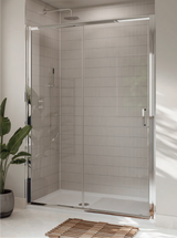 A modern sliding glass shower door installed in a tiled bathroom with a white walk-in shower, a wooden bath mat, and a potted plant.
